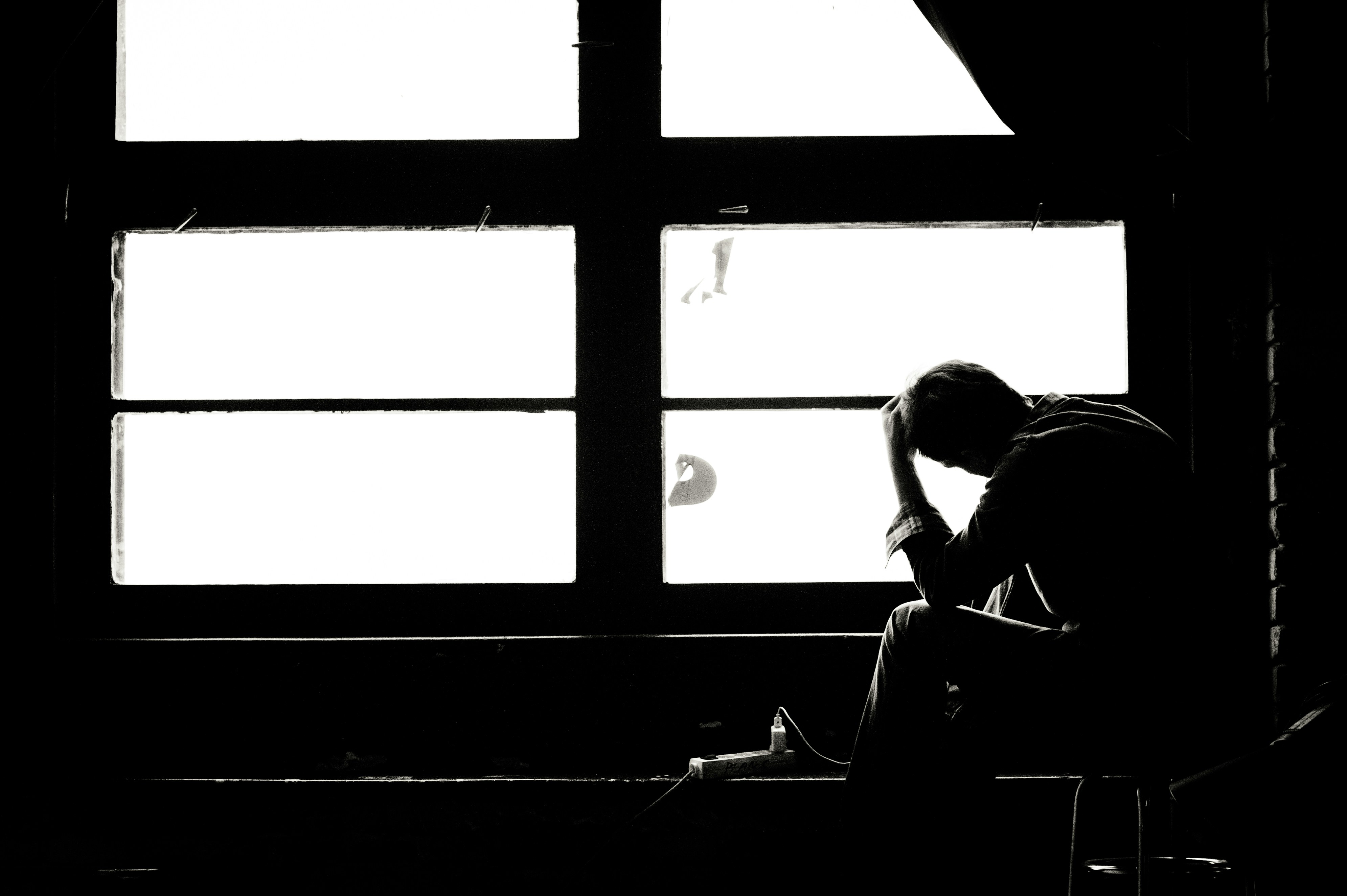 A man sitting quietly near a window, looking thoughtful and reflective, representing the emotional weight of infertility.