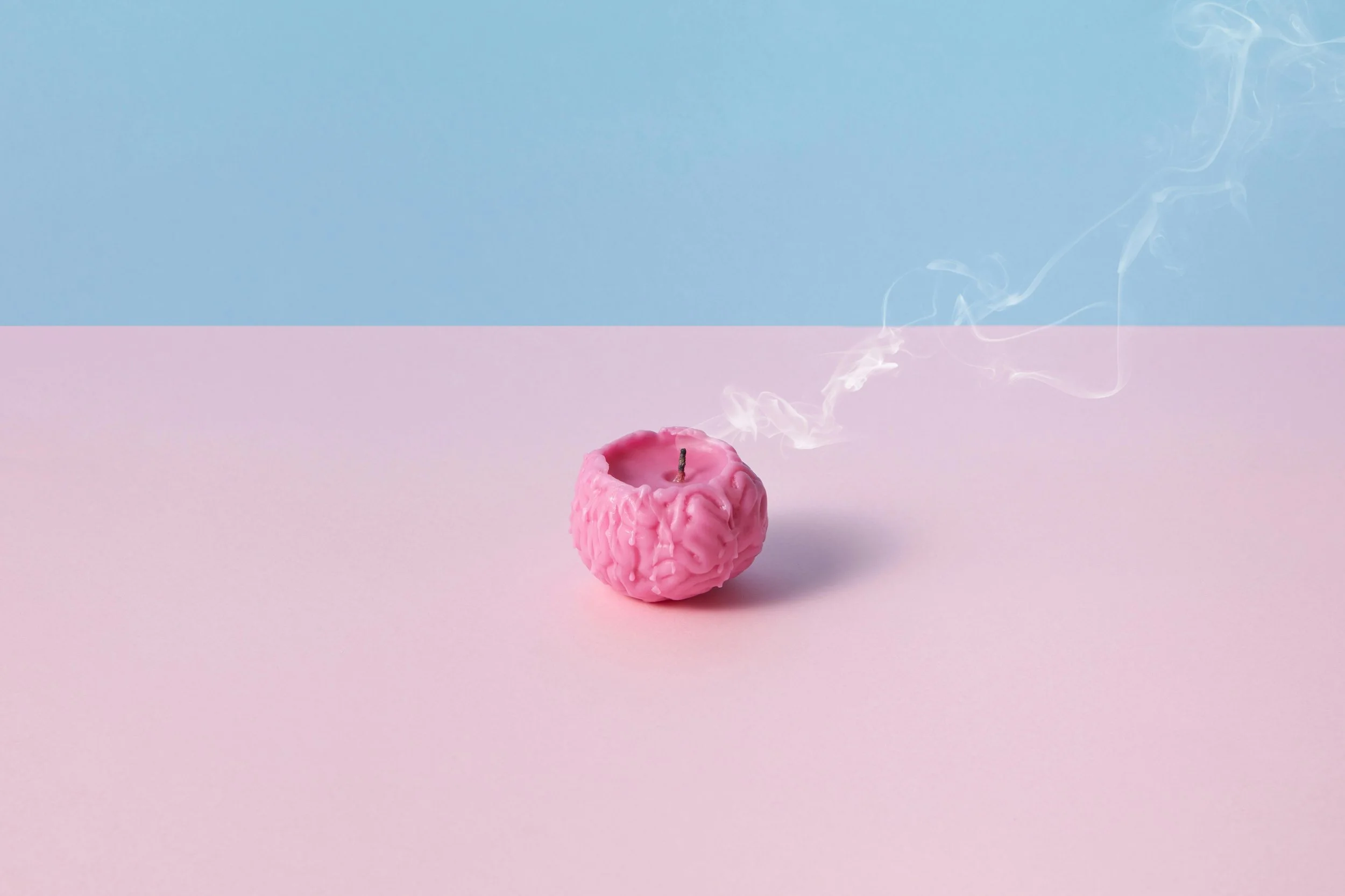 A brain-shaped candle with a wisp of smoke on a pastel pink and blue background